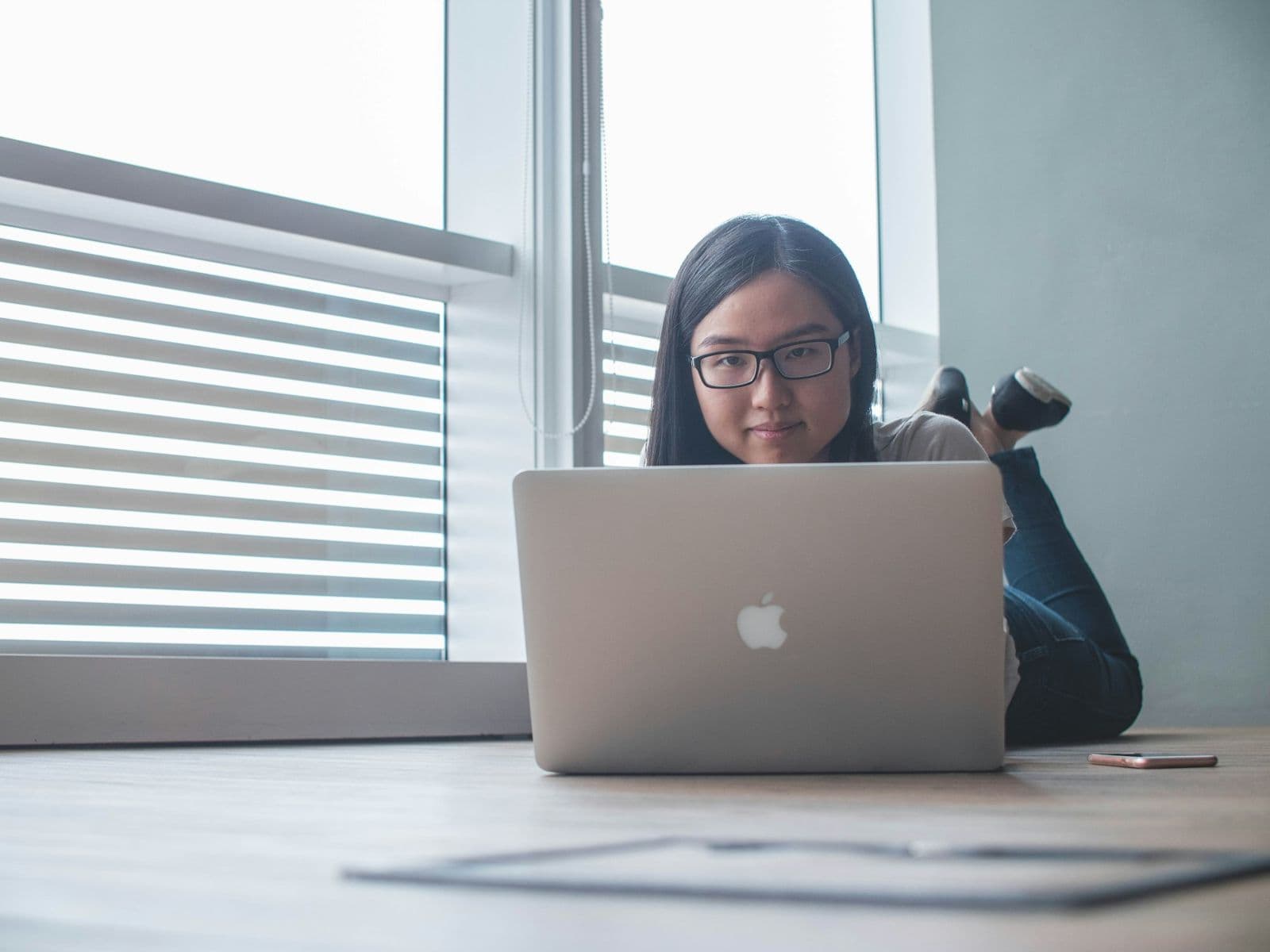 A woman focused on her laptop by a bright window